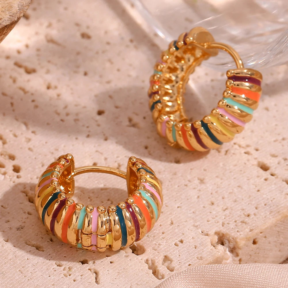 Gold hoop earrings with colorful stripes on a textured beige surface