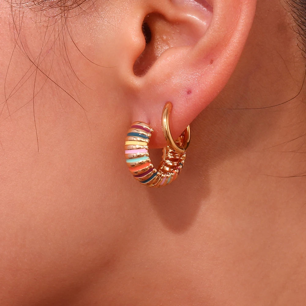 Close-up of an ear wearing a gold hoop earring with colorful stripes.