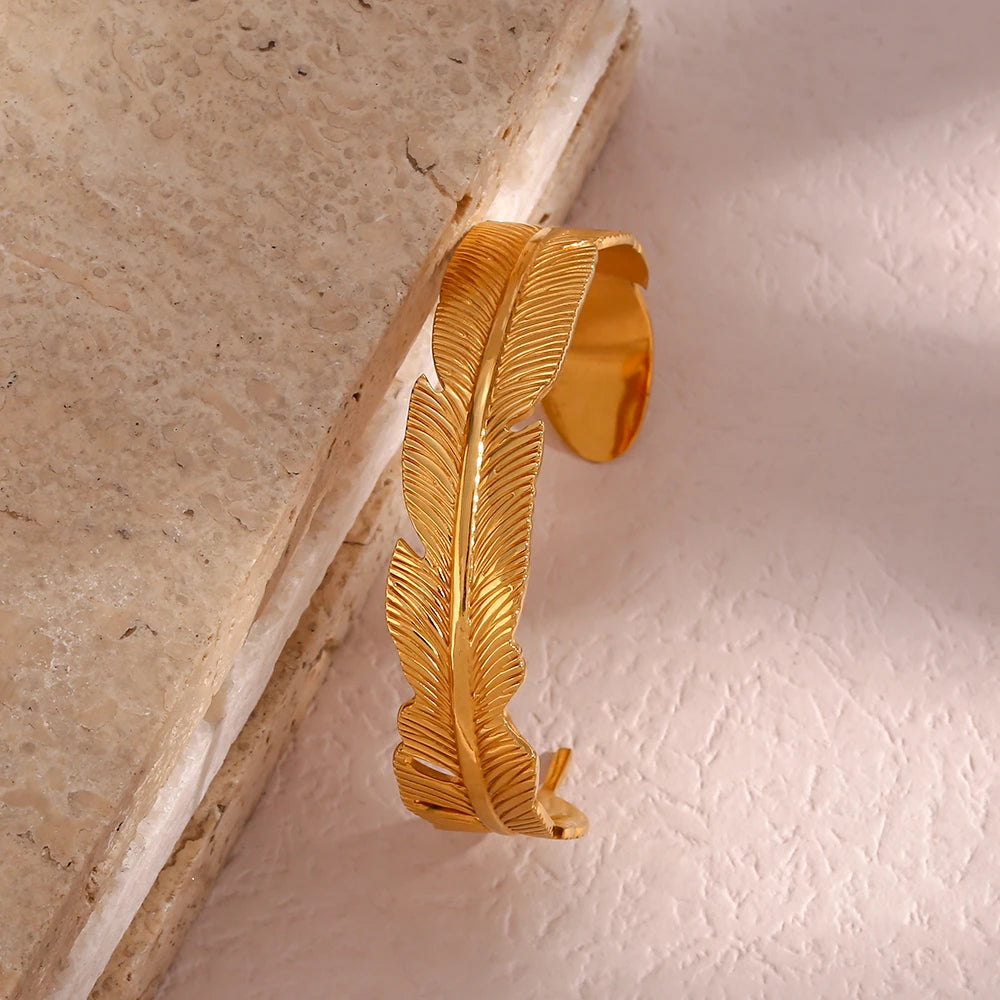 Gold feather-shaped decorative wall hook on a textured surface