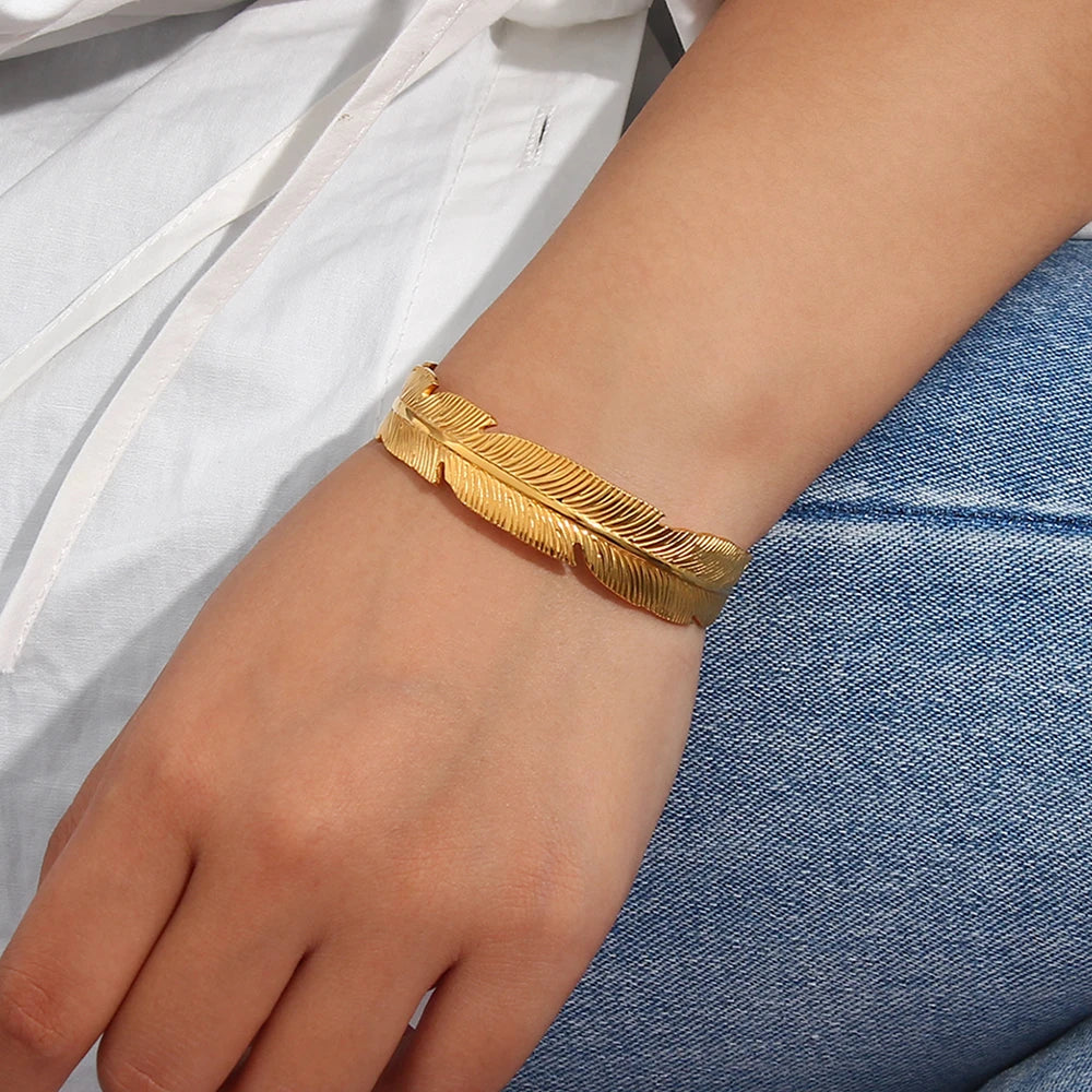 Gold feather bracelet on a wrist with a white shirt and blue jeans in the background