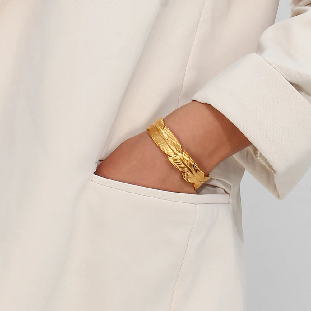 Gold feather bracelet on a person wearing a white outfit