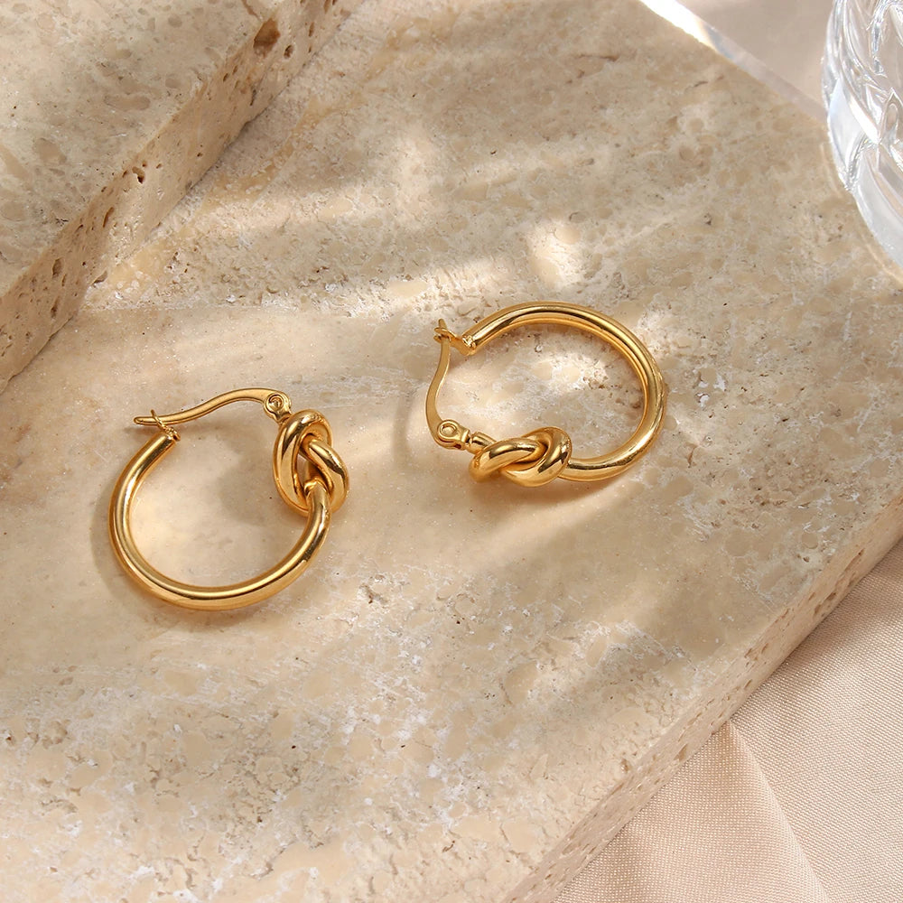 Gold hoop earrings on a beige stone surface