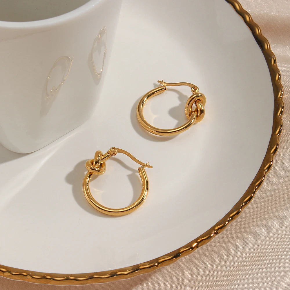 Gold hoop earrings on a white dish with a beige background