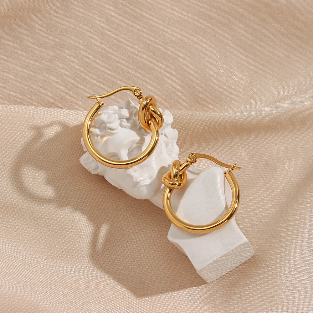 Gold hoop earrings with white stone on a beige fabric background