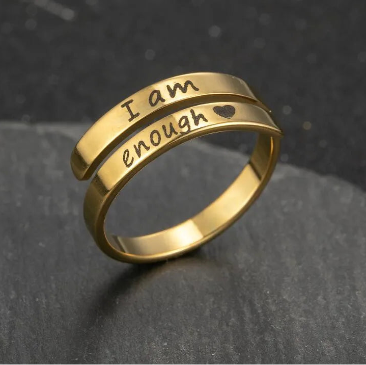 Gold ring with 'I am enough' engraving on a dark stone surface