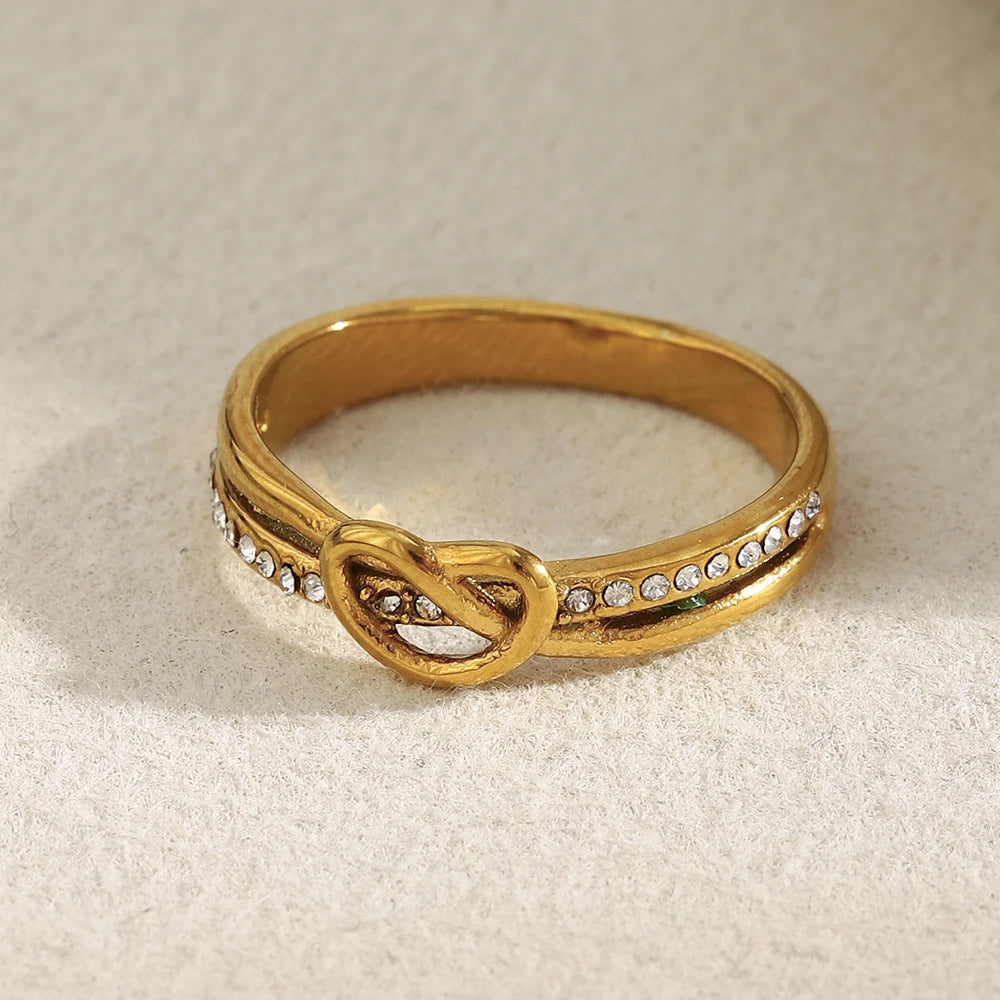 Gold ring with a knot design and small stones on a beige background