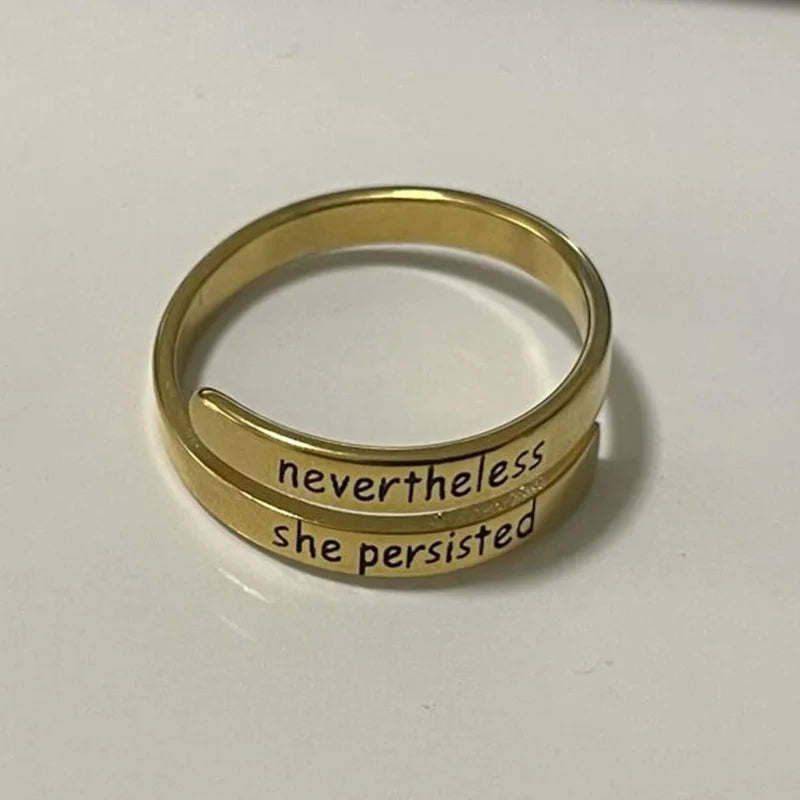 Gold ring with 'nevertheless she persisted' text on a white background