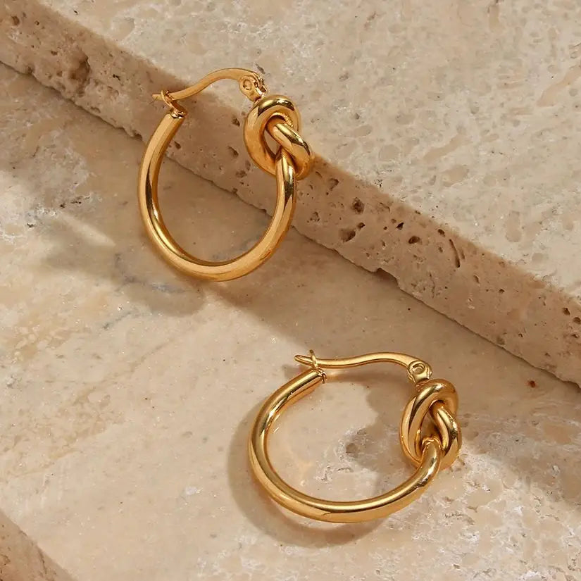Pair of gold hoop earrings on a beige stone surface