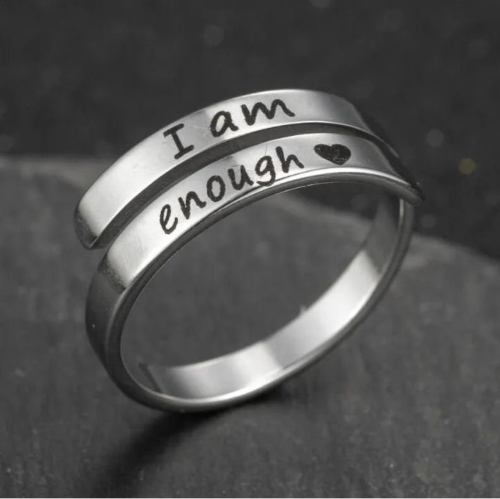 Silver ring with 'I am enough' engraving on a dark background