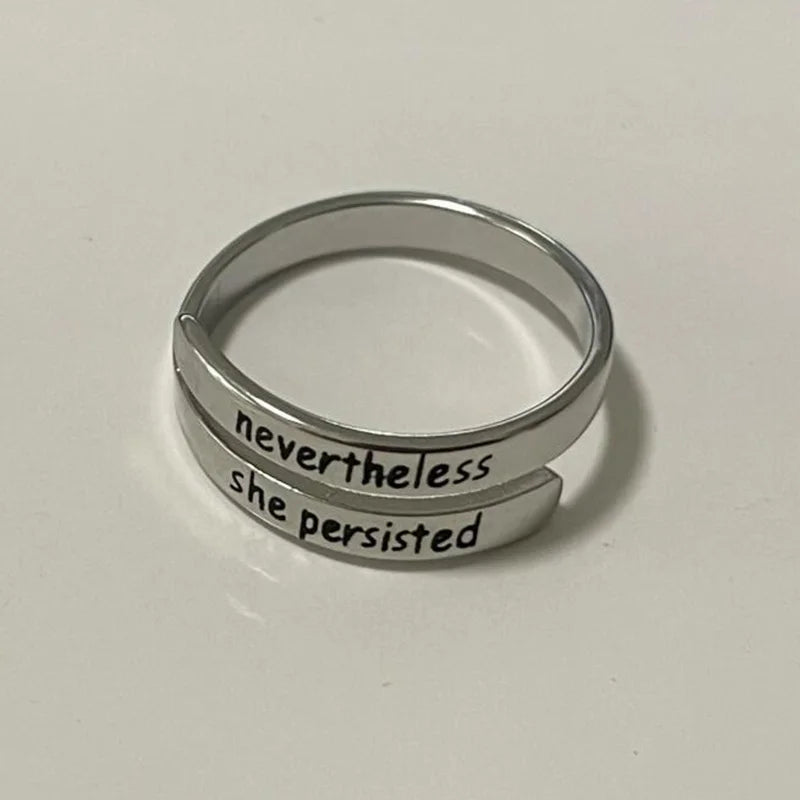 Silver ring with 'nevertheless she persisted' text on a light gray background