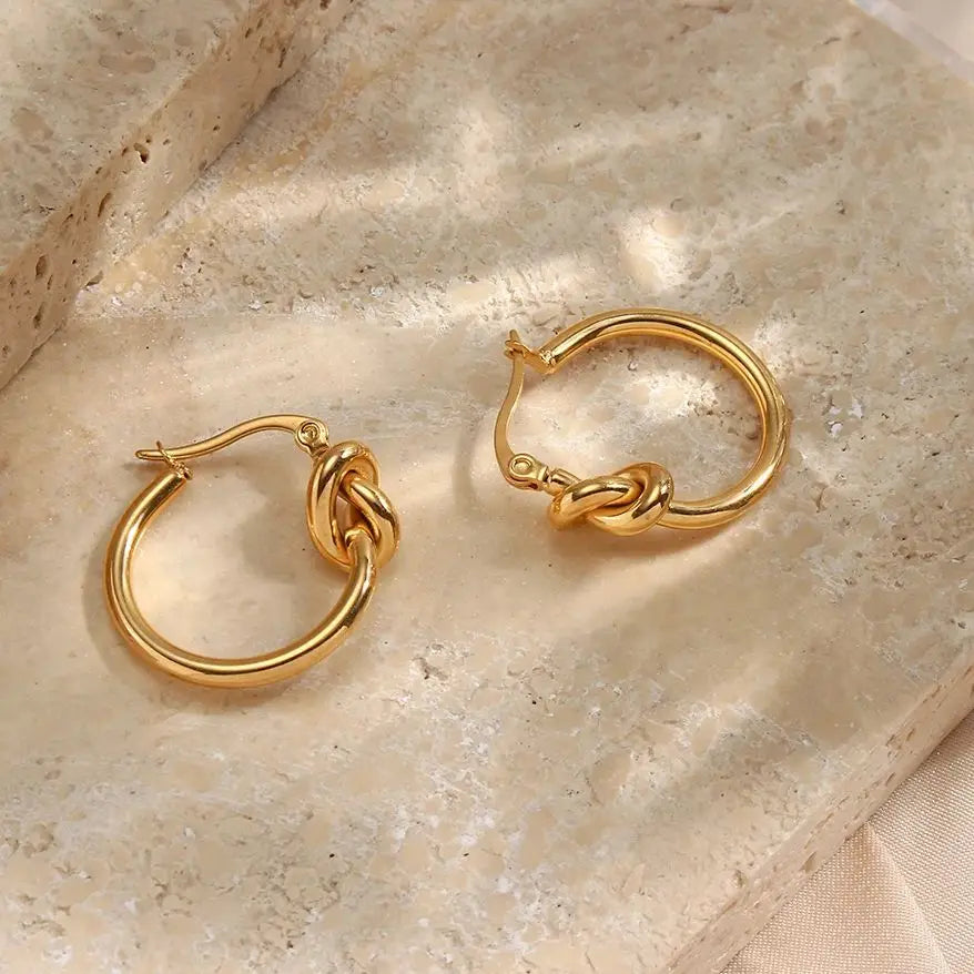 Gold hoop earrings on a beige stone surface