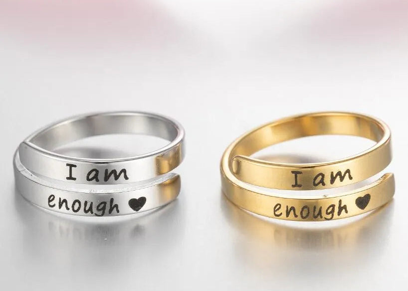 Two rings, one silver and one gold, with 'I am enough' engraving on a light background.