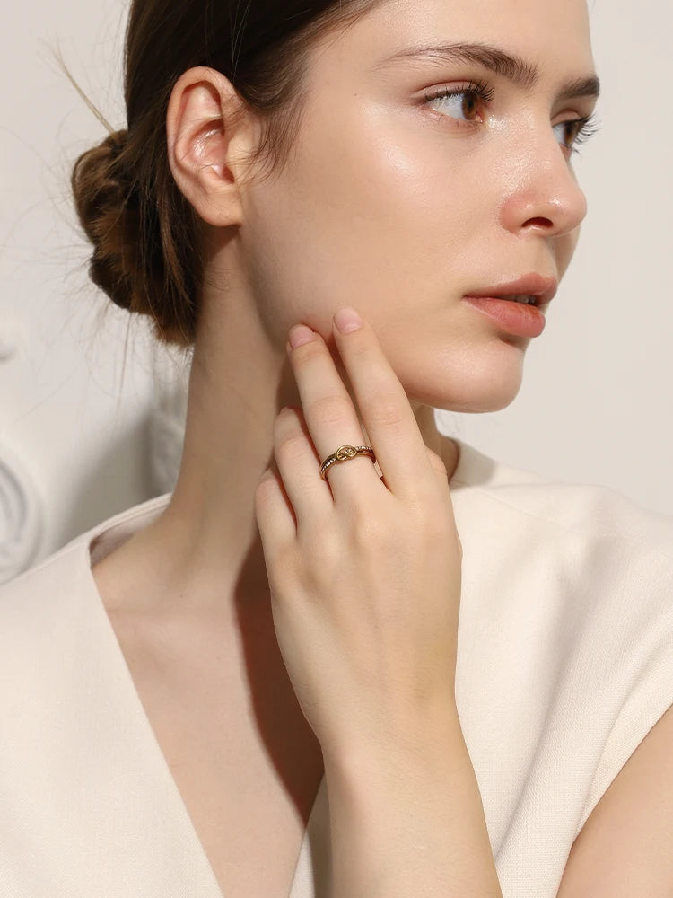 Woman wearing a gold ring on her finger, touching her neck against a neutral background