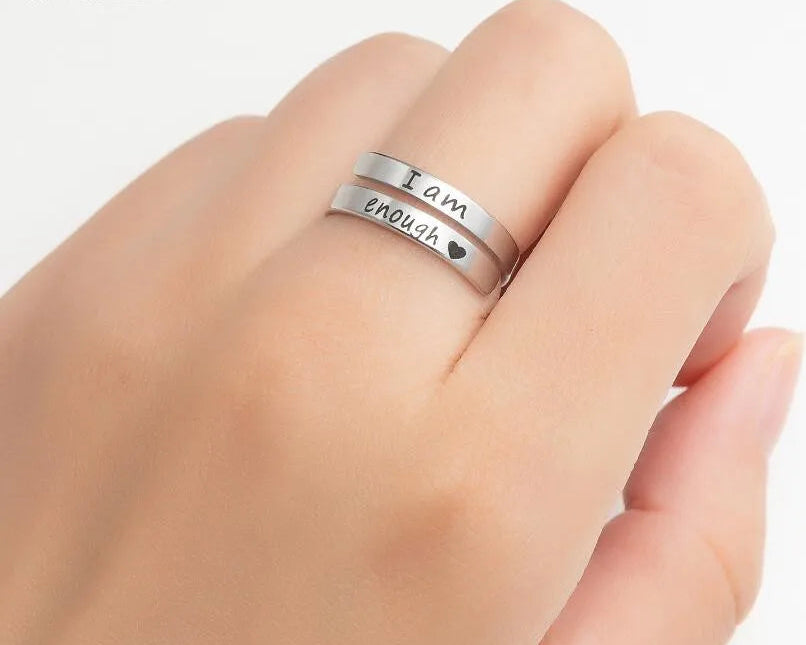 Silver ring with 'I am enough' engraving on a hand against a white background