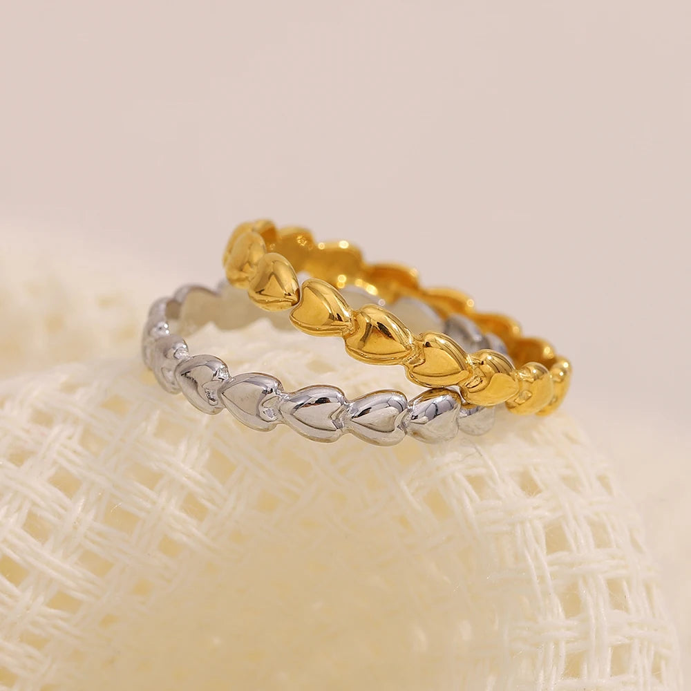 Two gold and silver heart-shaped rings on a textured beige surface