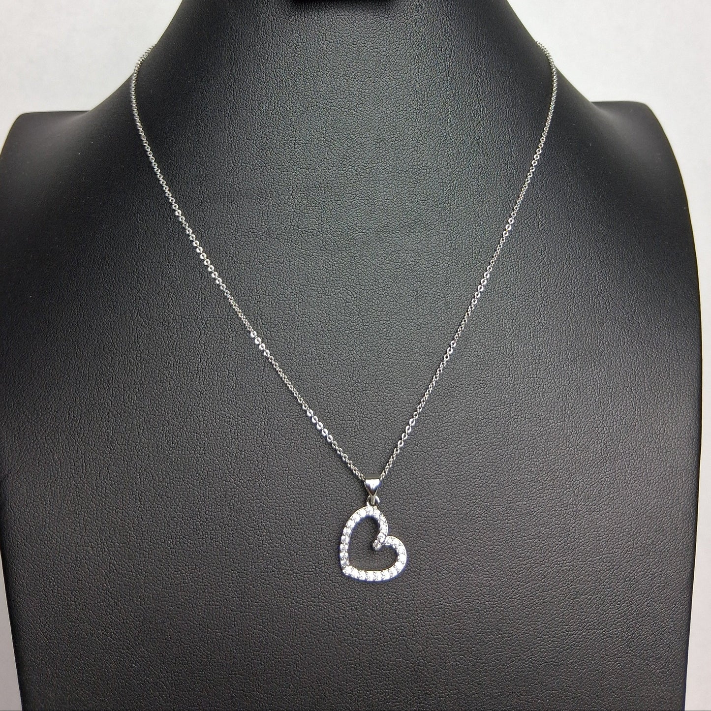 A white gold necklace with a heart-shaped pendant displayed on a black mannequin bust.
