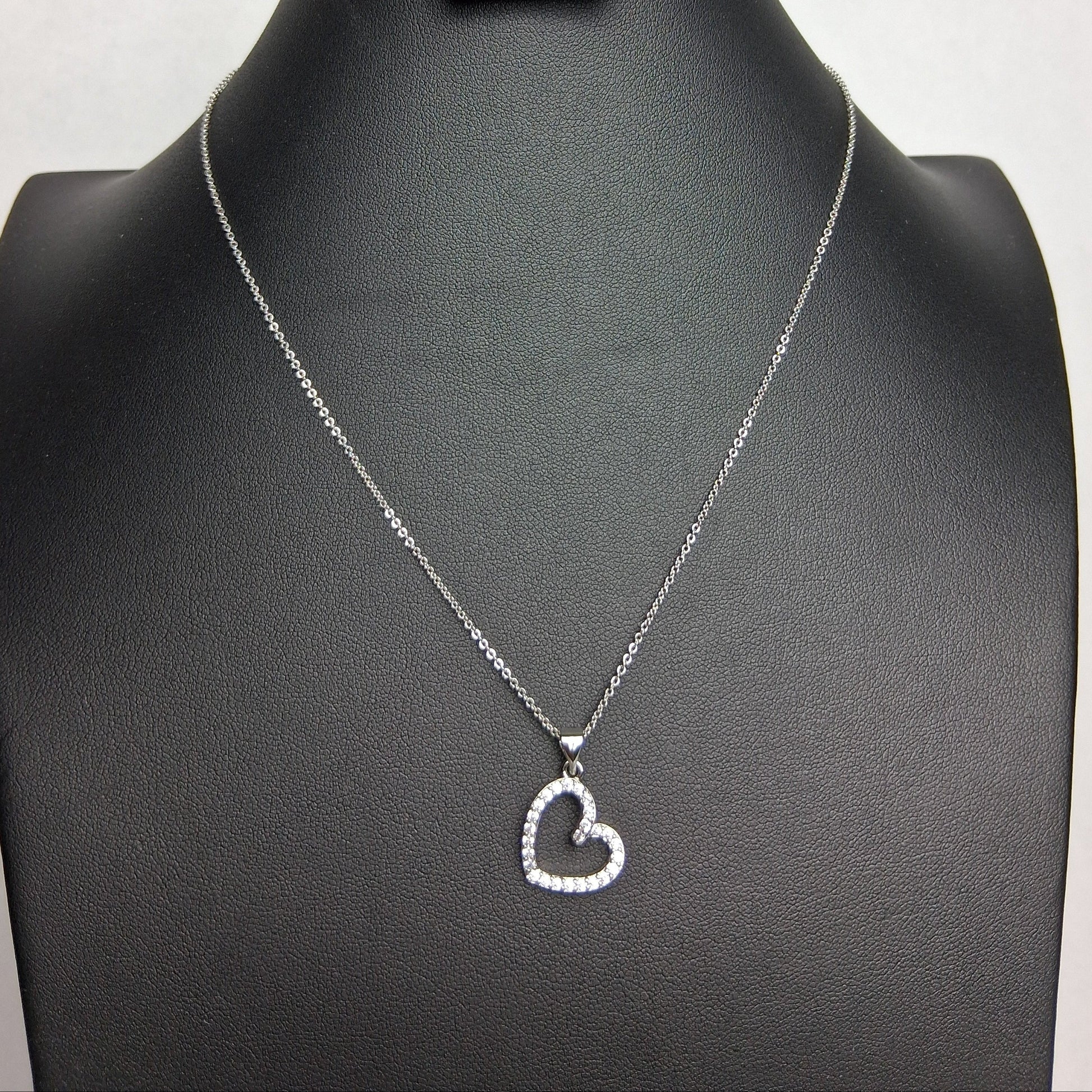 A white gold necklace with a heart-shaped pendant displayed on a black mannequin bust.